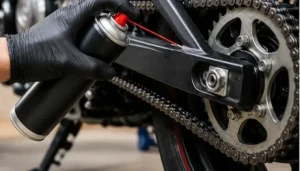 engrasar-cadena-moto-Mano con guante aplicando lubricante sobre la cadena y la corona de una moto