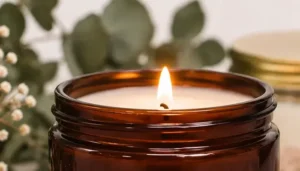 Vela aromática artesanal encendida en recipiente de vidrio ámbar